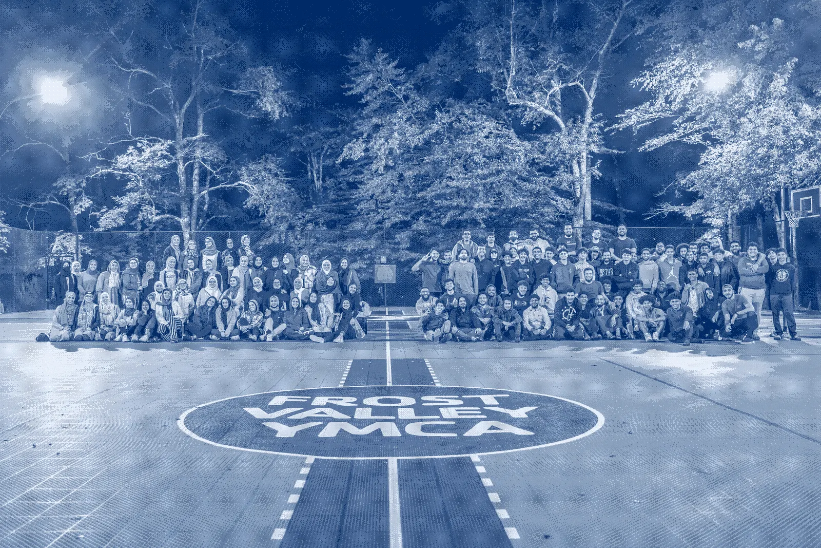 Dozens of young people gathered on a red basketball court at Frost Valley YMCA at night